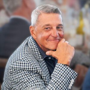 Phil Nardone, black and white plaid sport coat, sitting with hand resting on chin, looking over right shoulder